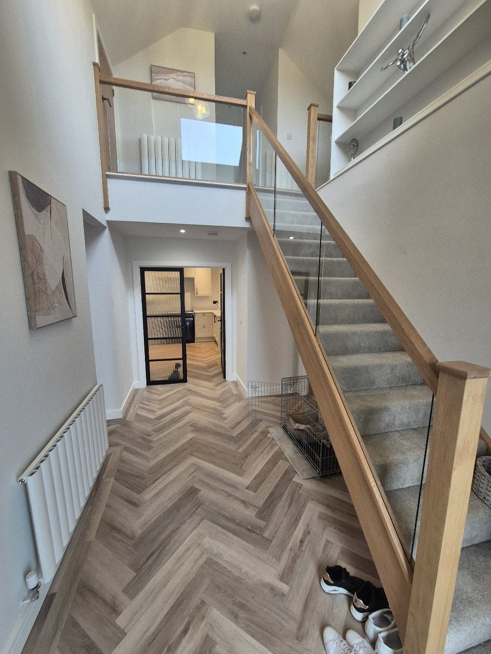 Finished staircase with grey carpet runner, glass balustrade, oak handrail and herringbone flooring